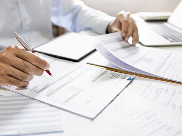 Professional hands reviewing financial records and laptop, marking documents during Asset Recovery investigation