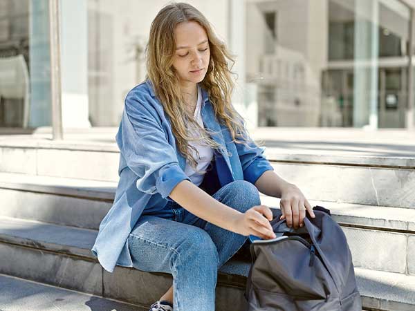 Teen girl sitting on steps searching a backpack, suggesting a runaway teenager in an urban setting