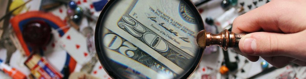 Magnifying glass over US bills and personal items, symbolizing asset investigations and recovery