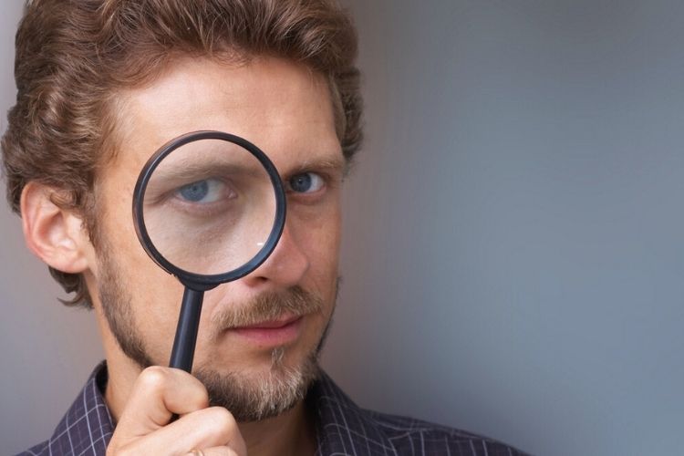 Investigator holding a magnifying glass to his eye, representing background checks for attorneys