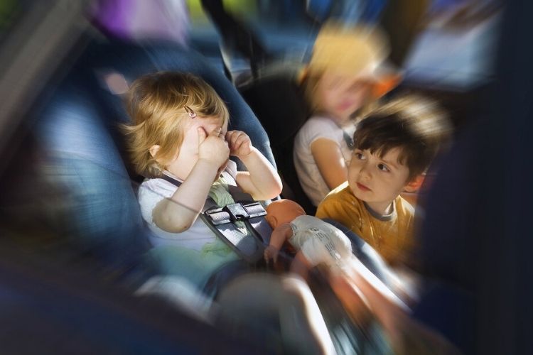 Two young children in car seats, one covering her eyes while another holds a doll — child protection investigation context