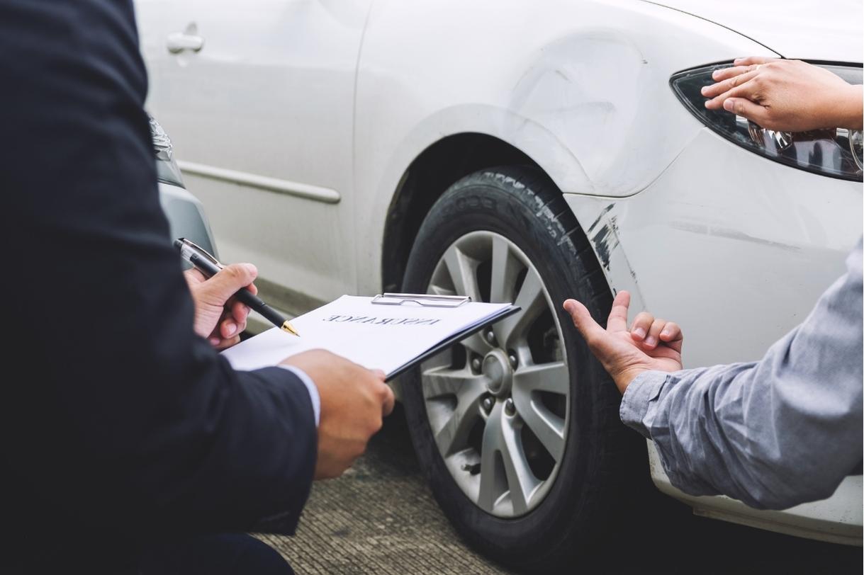 Investigator documenting damage on a scratched white car with clipboard during insurance accident investigation