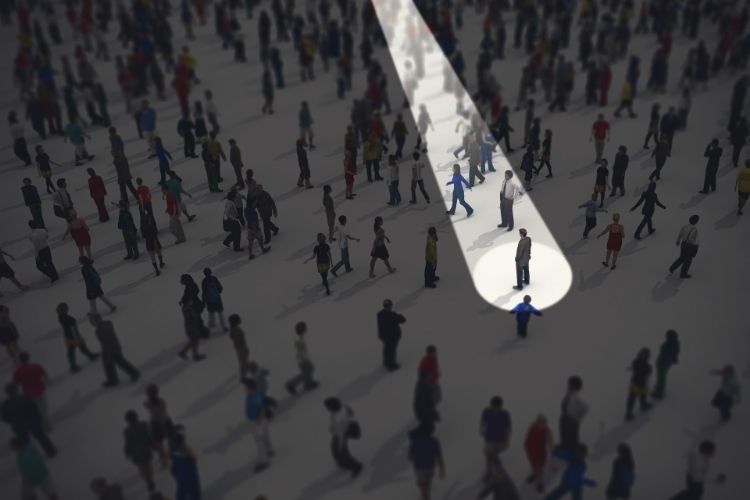 Spotlight highlighting one individual in a crowded scene, representing missing persons search and investigator services.