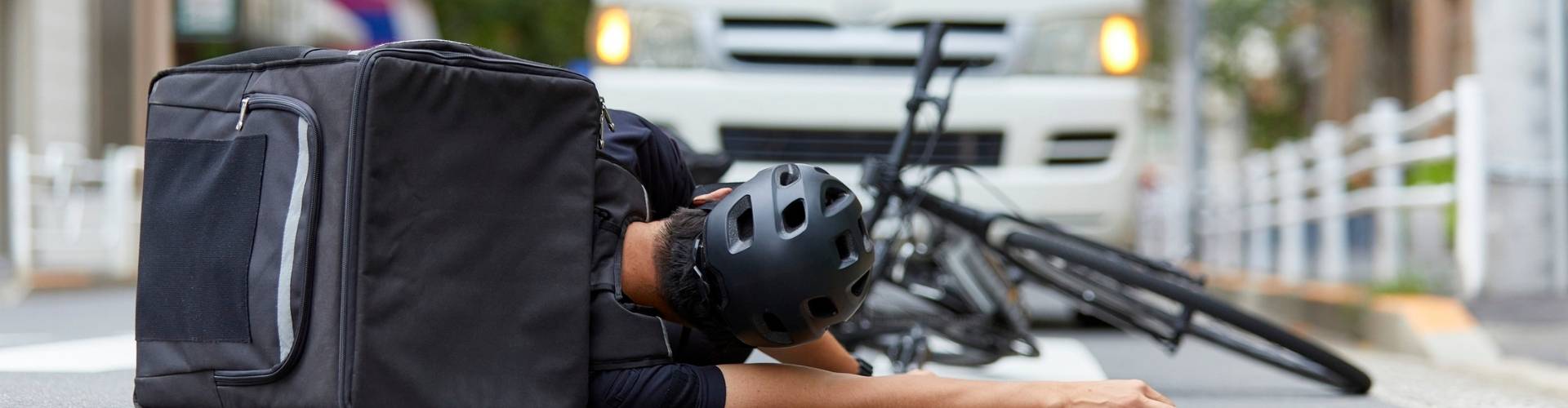 Fallen delivery cyclist beside bike and insulated bag near a vehicle, personal injury scene