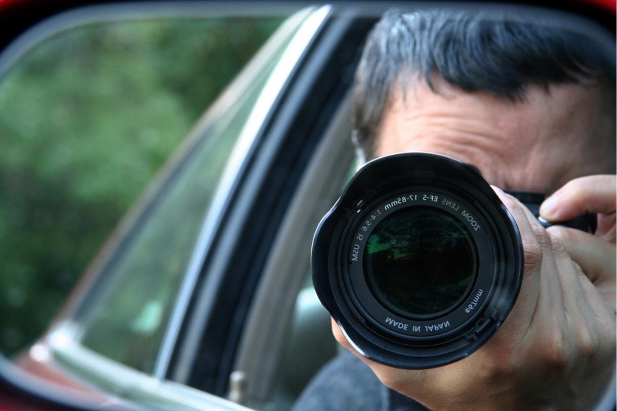 Investigator photographing from a car with a telephoto lens during process service surveillance