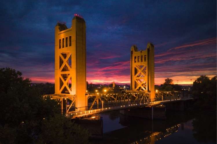 Tower Bridge in Sacramento lit at sunset, golden towers reflected on the Sacramento River