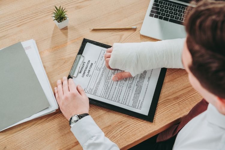 Person with arm cast reviewing workers' compensation claim form on clipboard at desk, illustrating AOE COE investigations