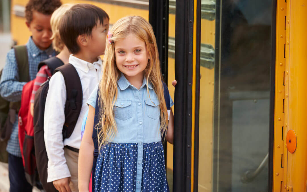 Smiling schoolgirl boarding a yellow bus with classmates — tip to help ensure your child doesn't go missing