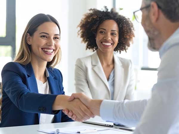 Two smiling investigators at a desk, one shaking hands with a client during a bilingual claims investigator meeting