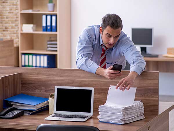 Man reaching over cubicle to take stacked documents while using phone — employee theft scenario