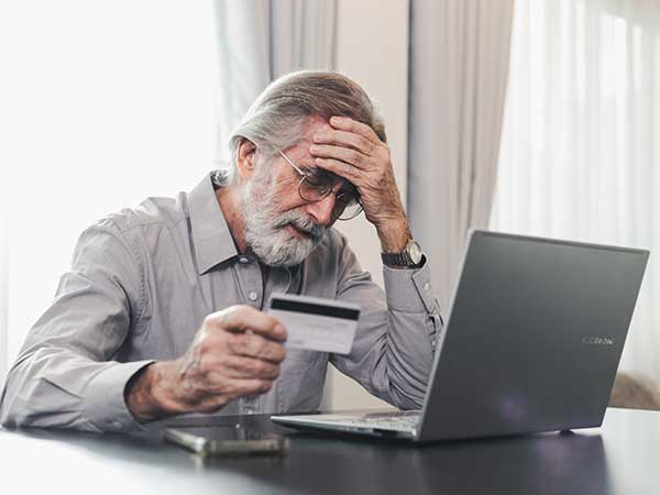 Elderly man at laptop holding a credit card, worried about fraud and scams