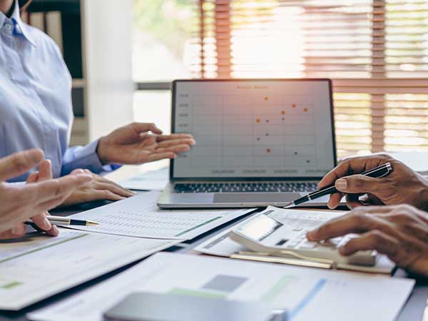 Hands pointing to documents, calculator and laptop chart during an intellectual property investigation meeting