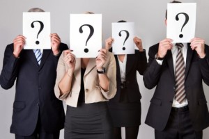 Four professionals in business attire holding question-mark signs over faces, illustrating uncertainty in a background check
