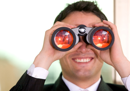 Businessman in suit using binoculars, representing corporate surveillance and private investigator services