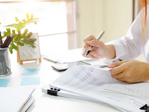 Hands reviewing financial documents and receipts at a desk, pen poised — asset investigations document review