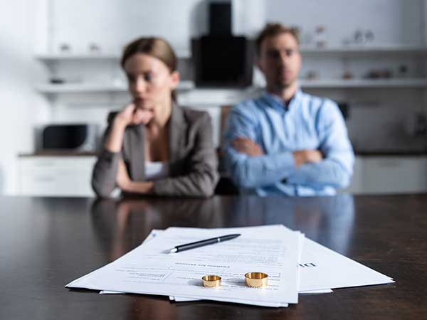 Divorce law investigations — divorce papers with two wedding rings and pen, estranged couple blurred in background