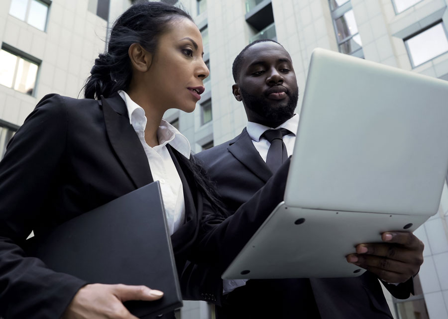 Two legal professionals reviewing case details on a laptop outside an office building